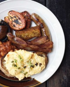 Breakfast meal with scrambled eggs, toast, sausages, tomatoes, and beans on a white plate