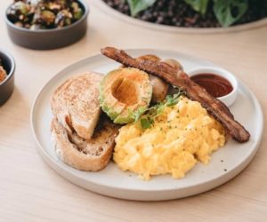Breakfast set with scrambled eggs, toast, avocados, and bacon on a white plate