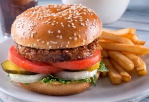 A vegan burger with tomatoes, pickles, and onions with fries on the side
