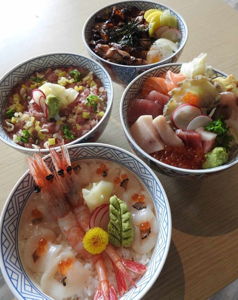 Four bowls of assorted Japanese dishes with raw fish, prawns, and vegetables