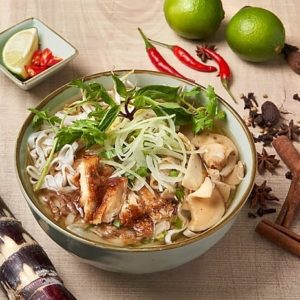 A bowl of Vietnamese pho with chilies, lime, and garnish