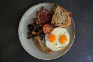 A big plate of English breakfast with sunny side up eggs, toast, tomatoes, bacon, and sausage