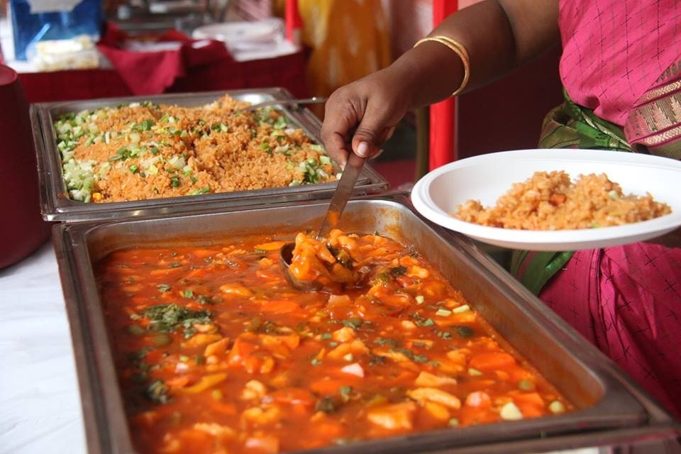 A woman scooping Indian food on a plate buffet-style
