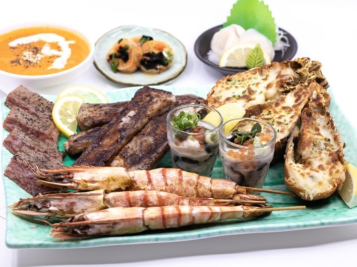 A plate of assorted grilled meat, prawns, steak, and sides